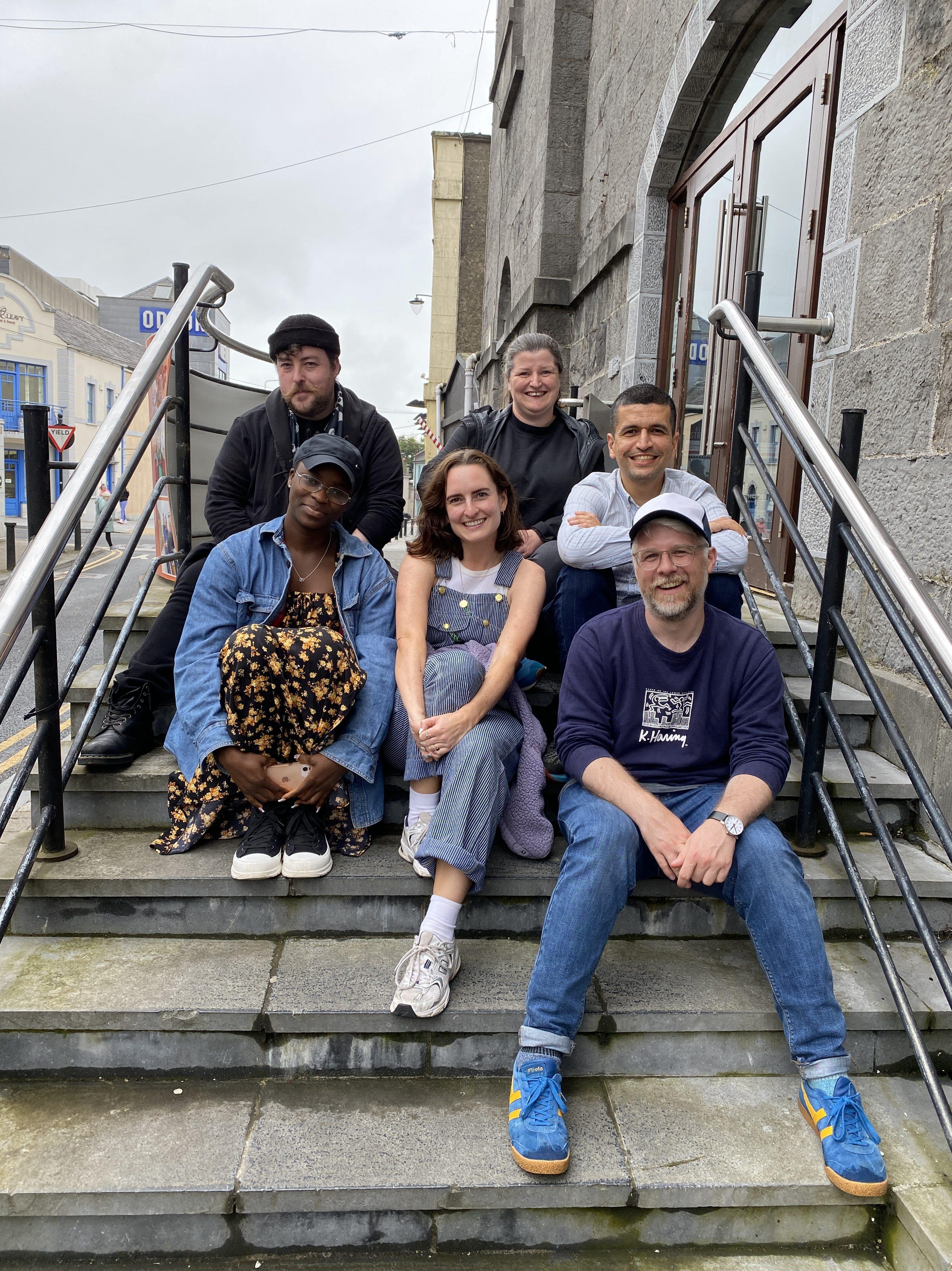 Finbarr Doyle, Olamide Mariam Oladapo, Maeve O’Mahony, Kate Heffernan, Shadaan Felfeli and Eoghan Carrick sitting on the steps of Dunamaise Arts Centre